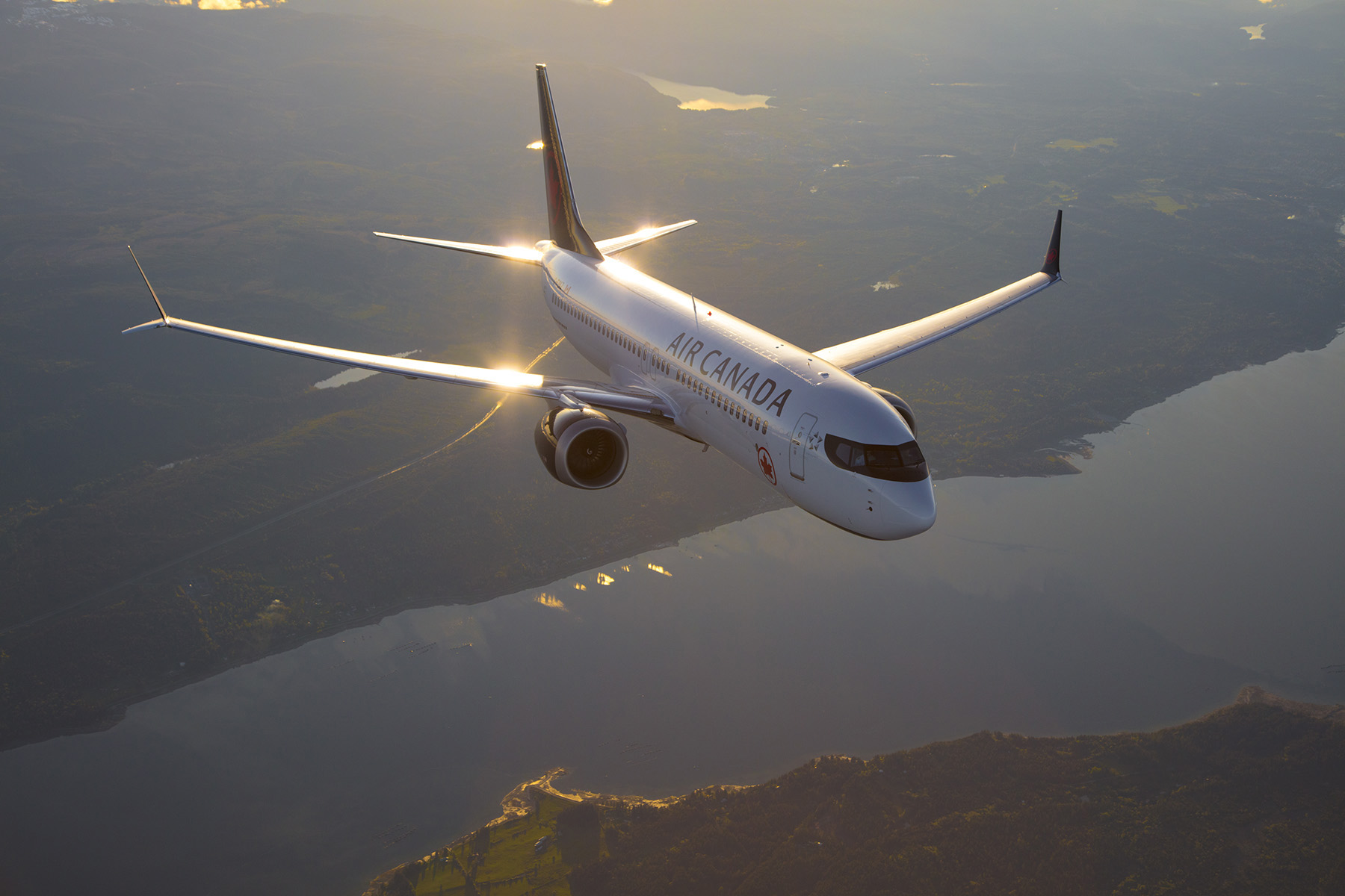 B737 Max flying over a river with the sun reflecting on the plane's surface